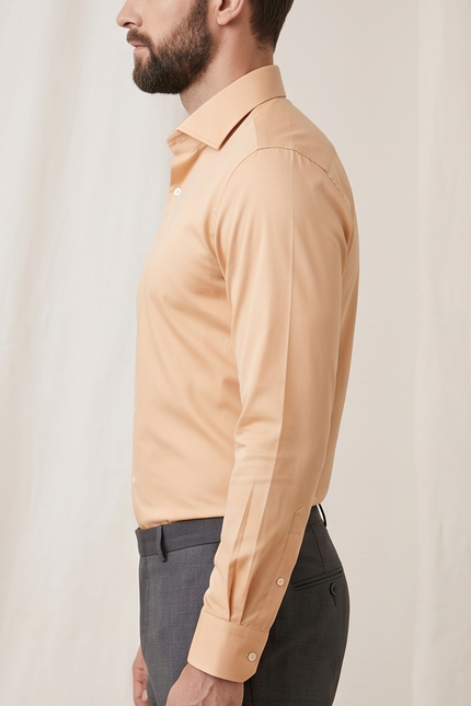 Man wearing a beige dress shirt and dark pants against a plain background