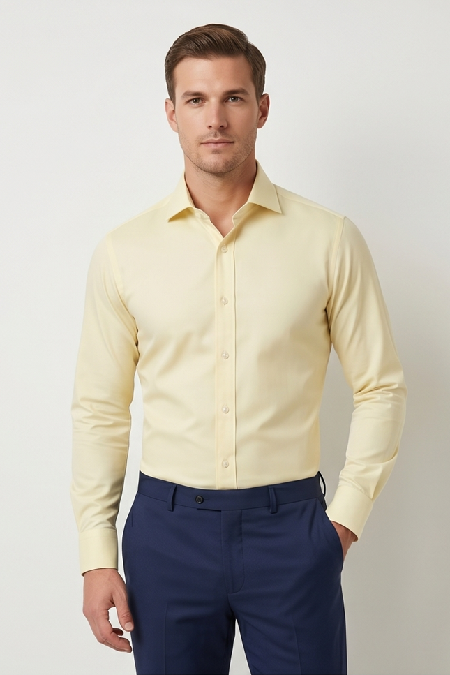 Man wearing a light yellow dress shirt and navy pants against a plain background