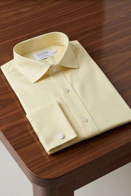 Folded light yellow dress shirt on a wooden surface with 'KAMU' label.