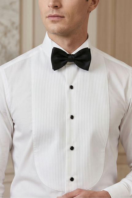 A man wearing a white pinstriped formal tuxedo vest with black buttons, a white dress shirt, and a black bow tie, shown from the chin down against a soft beige background.