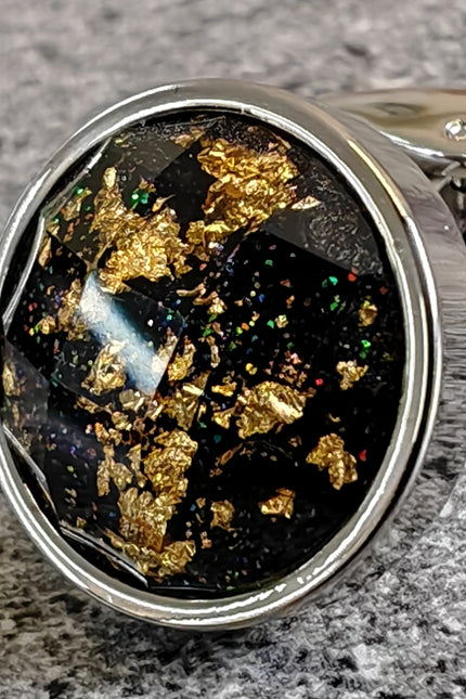 Close-up of a cufflink with black stone and gold flakes on a gray surface